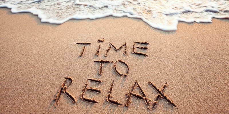 "Time to relax" written in the sand on the beach